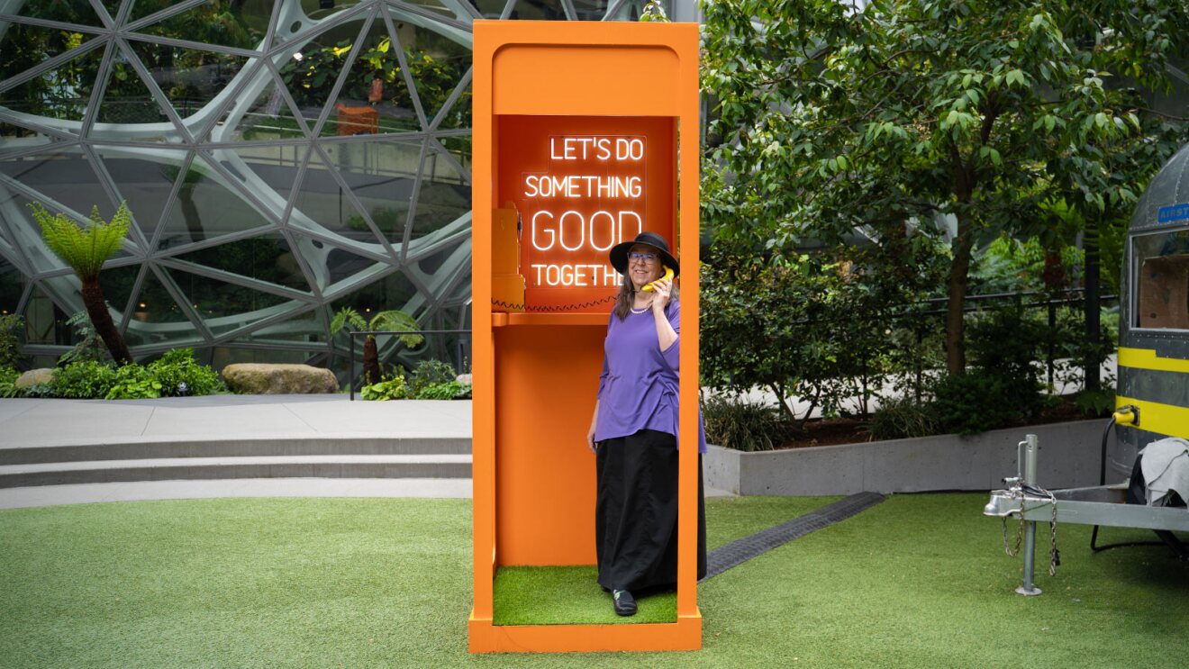 Person in purple shirt using bright orange phone booth with inspirational sign