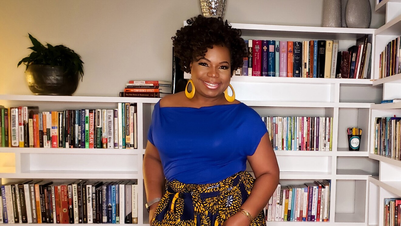 An image of a woman smiling for a photo in front of her bookcase.