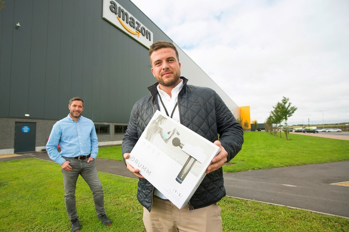Business owner stood in front of Amazon fulfilment centre holding product in a box