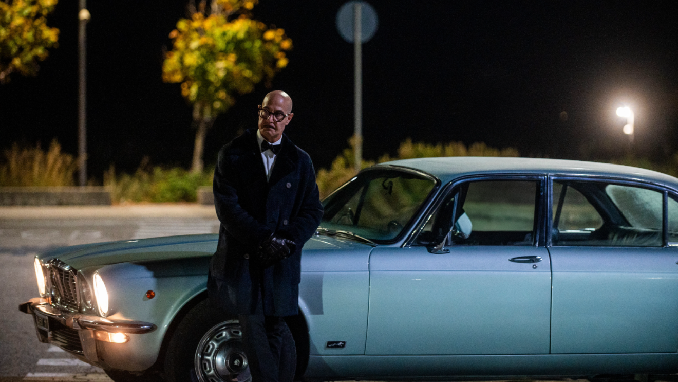 Stanley Tucci stands by a car in Prime Video movie Masterplan