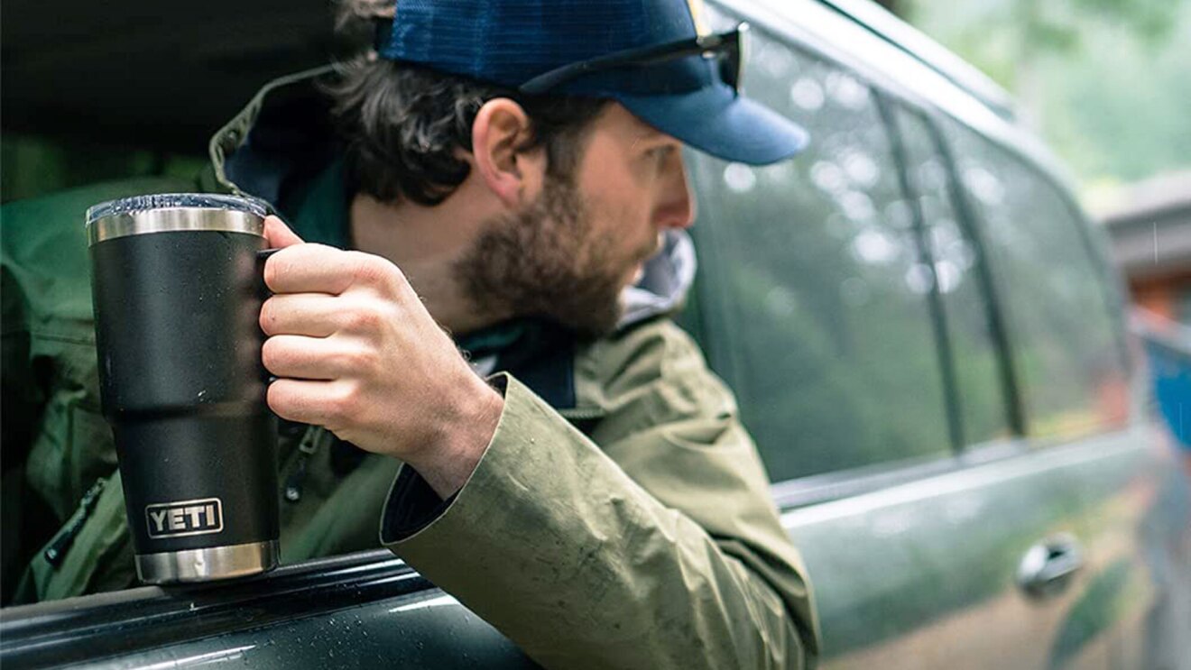 A man holds his YETI mug as he sticks his head out the window to reverse his SUV.