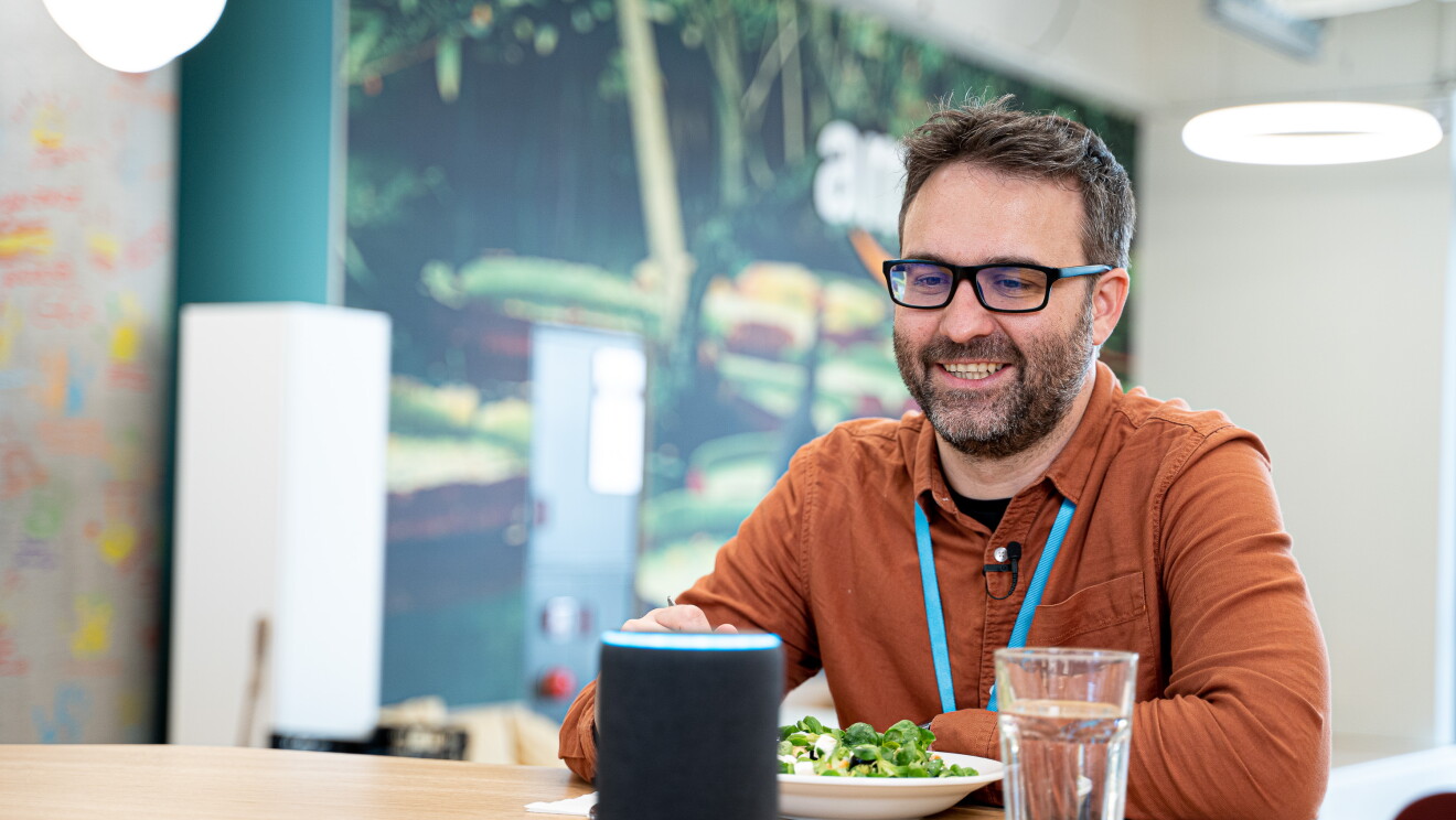 Daniel Méndez, Content Program Manager de Alexa comiendo una ensalada y con un vaso de agua en una mesa. Enfrente de un altavoz inteligente Amazon Echo.