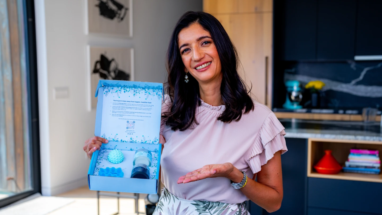 Paola Ramirez-Shah smiling and holding a box of Tucketts wellness accessories including a spiky massage ball.