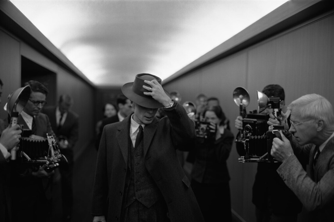 A black and white image of a man in a wide brimmed hat surrounded by cameras