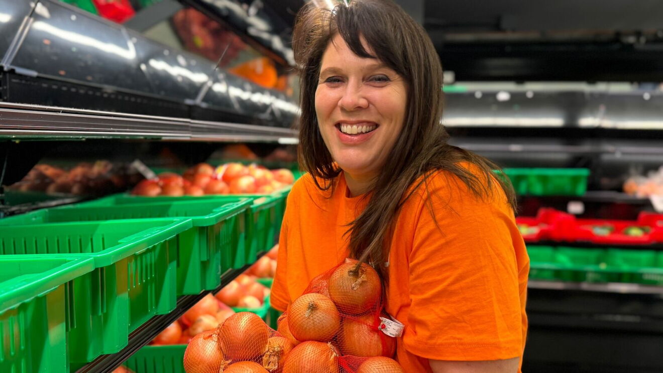 Smiling woman in orange volunteer shirt holding bag of onions in produce section