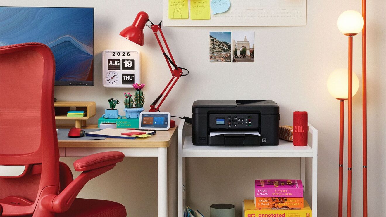 Modern home office workspace with red ergonomic chair, wooden desk, printer, and red task lamp