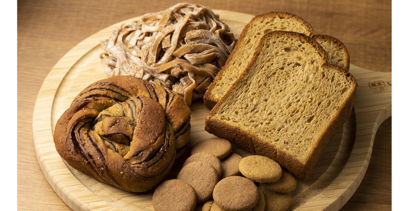 チョコレートが練りこんであるパンと、色が濃い食パン、クッキー、パスタとさまざまなスタイルの商品が並ぶ写真