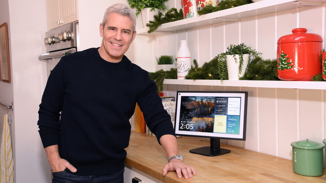 Andy Cohan wears a black sweater and stands in his holiday-decorated kitchen next to his Alexa.