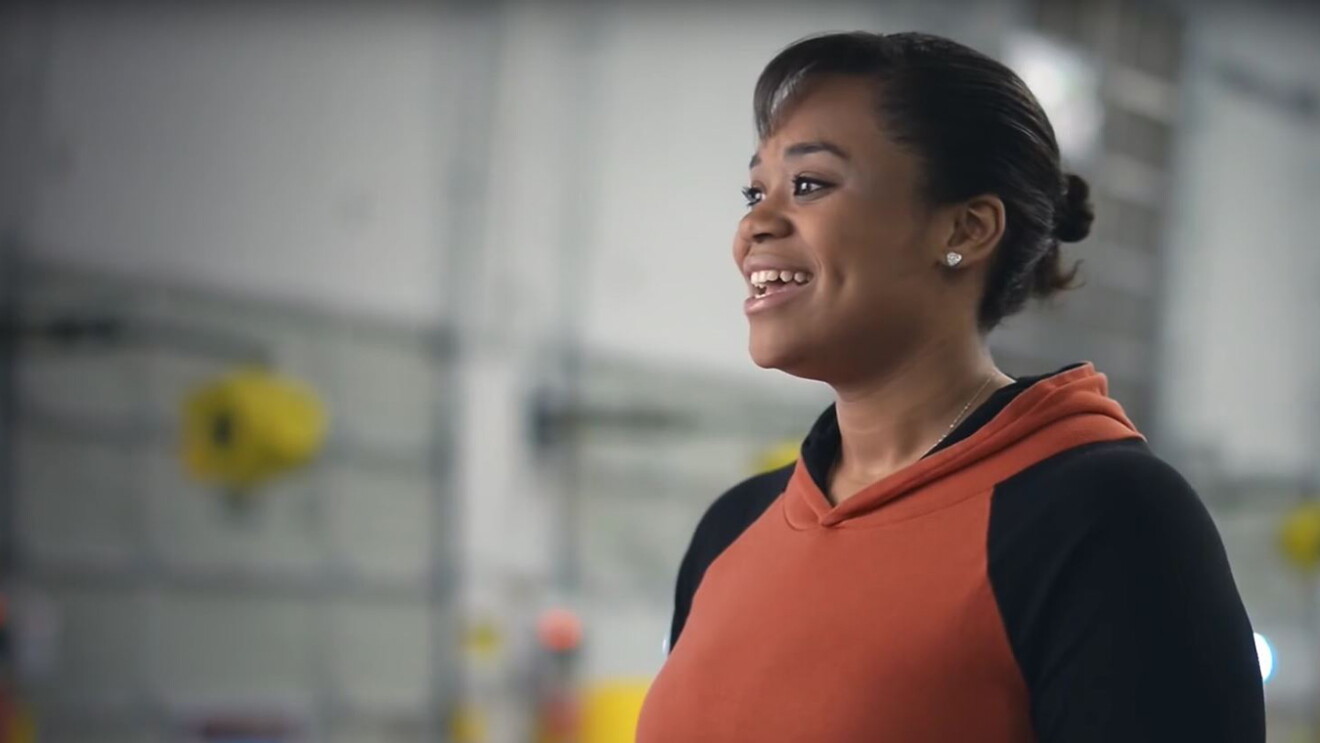 A young woman in an Amazon fulfillment center smiles, as she looks to the right of the camera. 