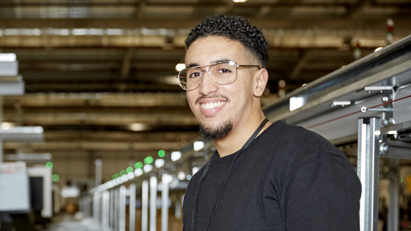 A close up photo of Imad smiling at the camera inside an Amazon warehouse
