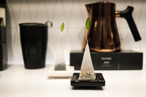 Tea is visible inside a pyramid-shaped teabag adorned with a green, leaf-shaped label.