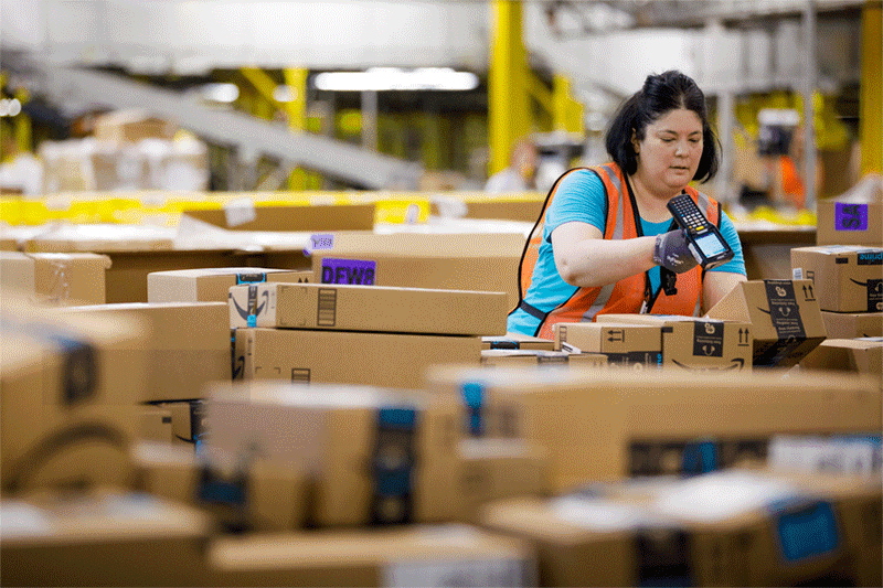A woman working in an Amazon fulfillment center scans boxes.