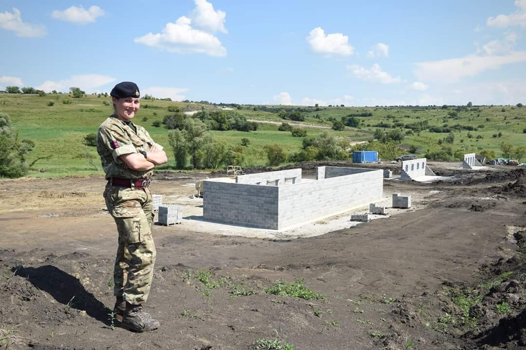 Reservist, Sophie Martin, standing cross-armed and dressed in her Army uniform with an outdoor military facility in the background.