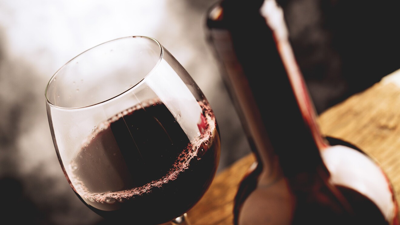 A glass of red wine and wine bottle on a rustic table.