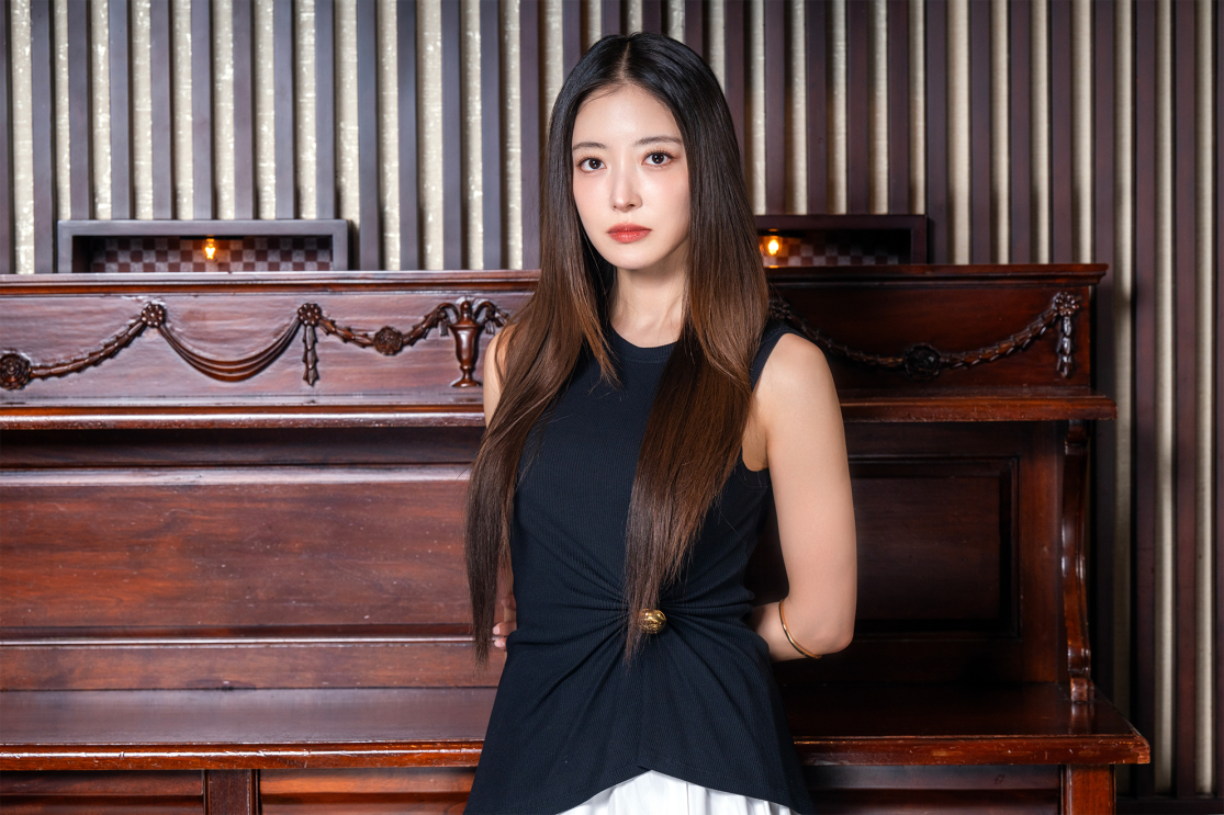 長いストレートヘアの黒いドレスを着ている女性(イ・ヨセンさん)が、エレガントな装飾が施された部屋でテーブルの前に立っている。