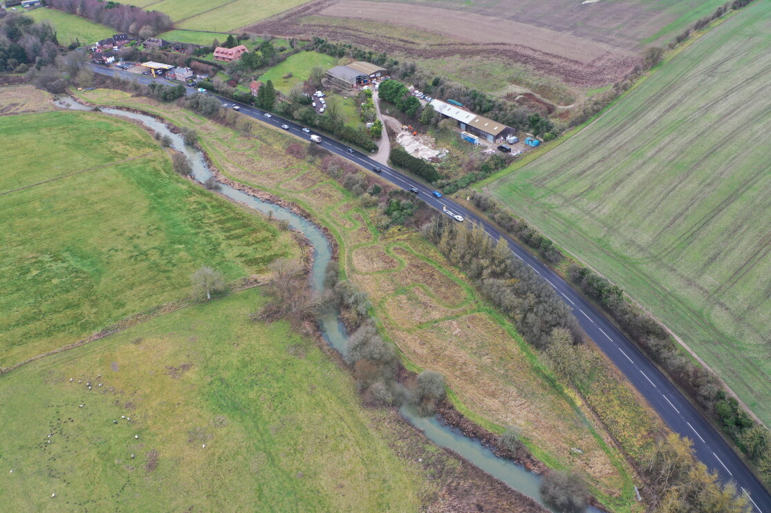 Aerial view of winding river alongside rural road and farmland