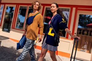 An image of two college students walking out of a store and looking at the camera. They are wearing colorful outfits.  