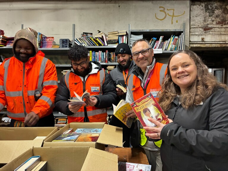 A group of employees in a fulfilment centre smiling and holding books 