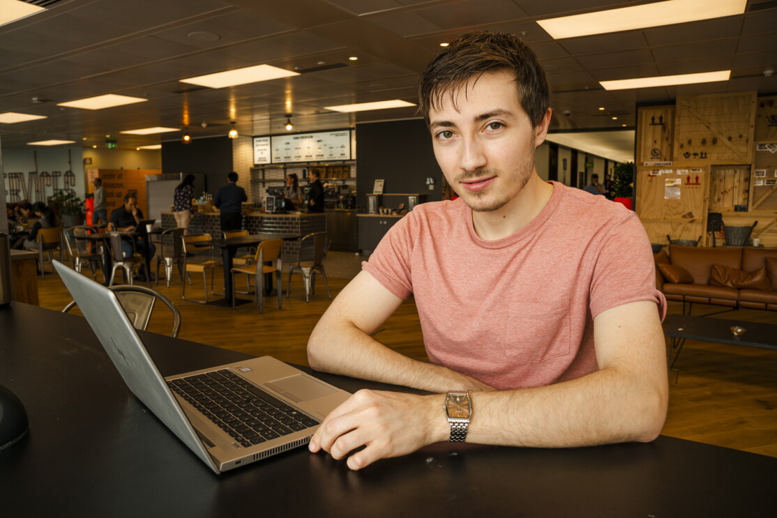 Jake Peters, 23, an  Infrastructure Technician apprentice sitting in the UK Amazon corporate office cafeteria behind a laptop. 