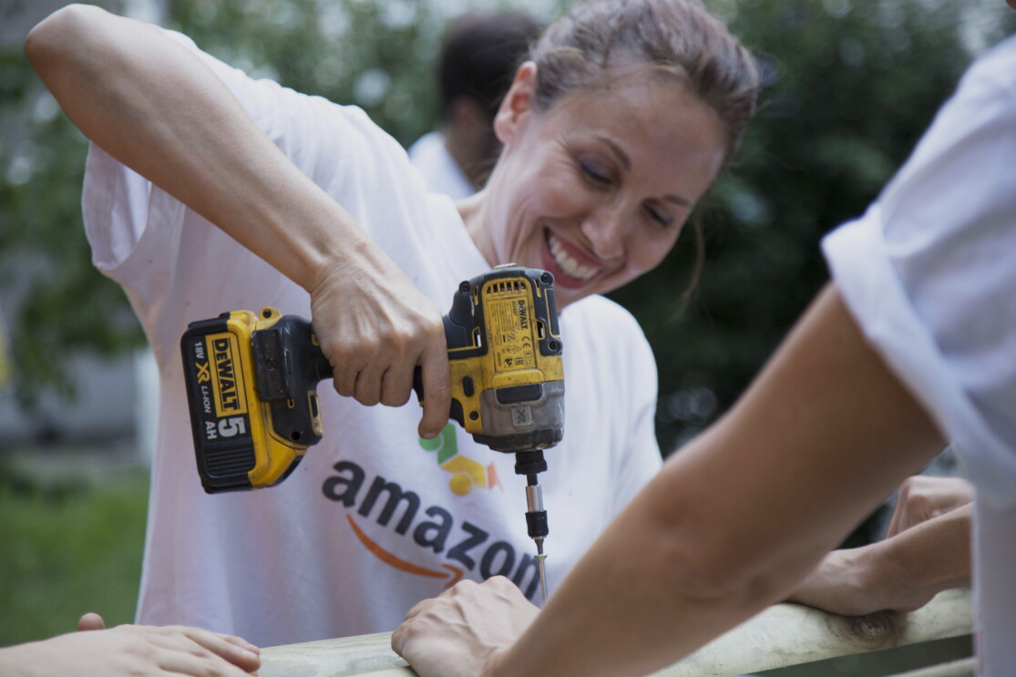 Volontaria di Amazon sorride in primo piano mentre regge un trapano durante i lavori alla Scuola Media Leonardo da Vinci di Affori, nella periferia di Milano.