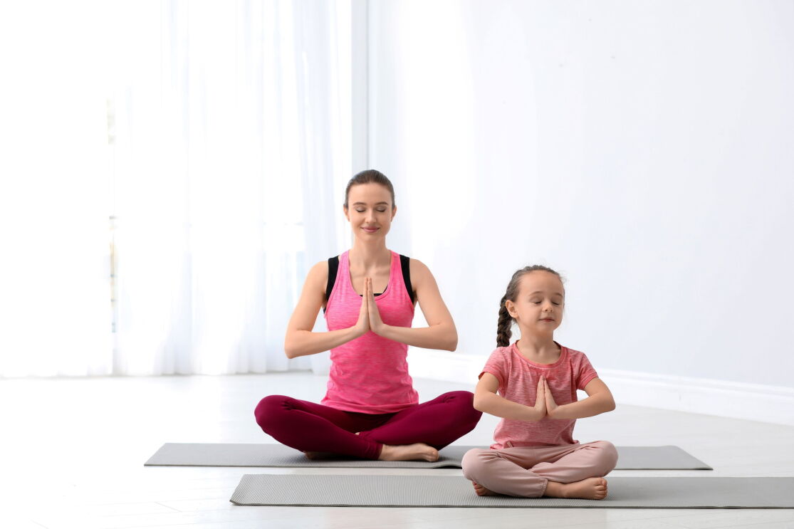 A mother is doing yoga with her daughter in pink shirts
