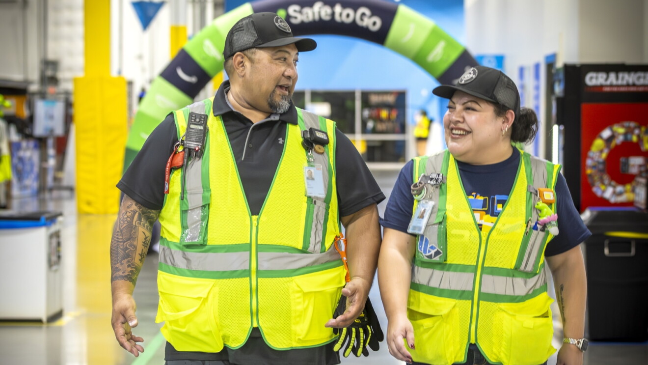Two smiling Amazon workers in safety vests under 'Safe to Go' sign