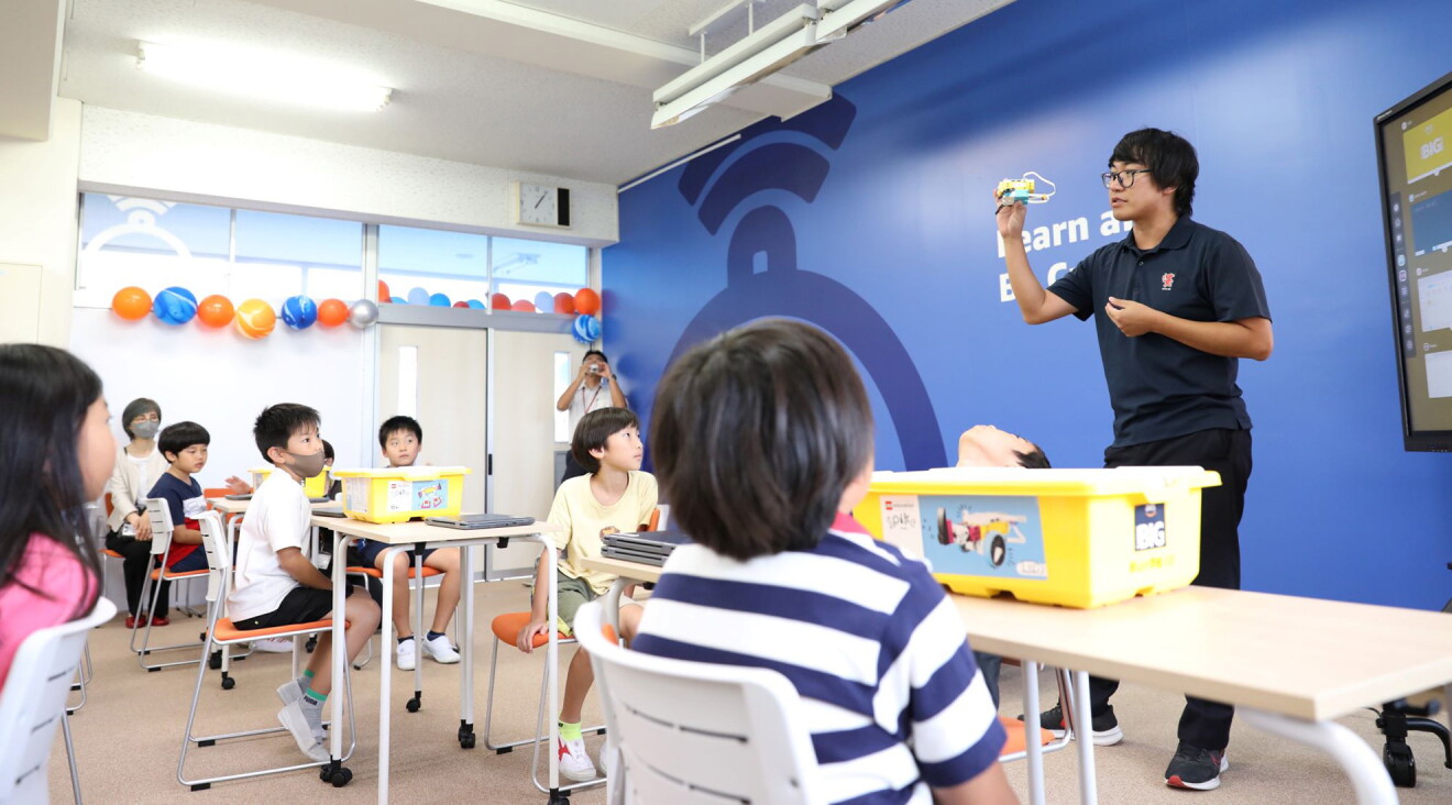 ロゴブロックを手に説明をする先生とそれを聞いている子どもたち