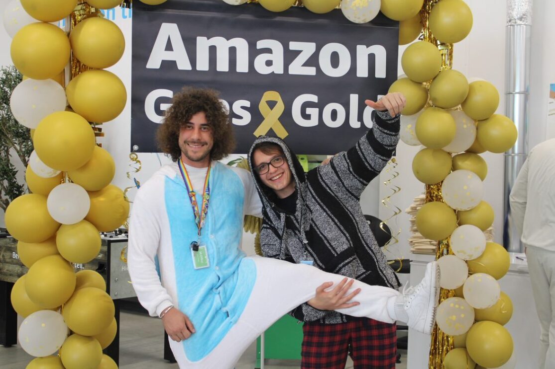 Zwei Mitarbeiter:innen aus dem Amazon Logistikzentrum Gera stehen vor dem „Amazon Goes Gold“ Banner.