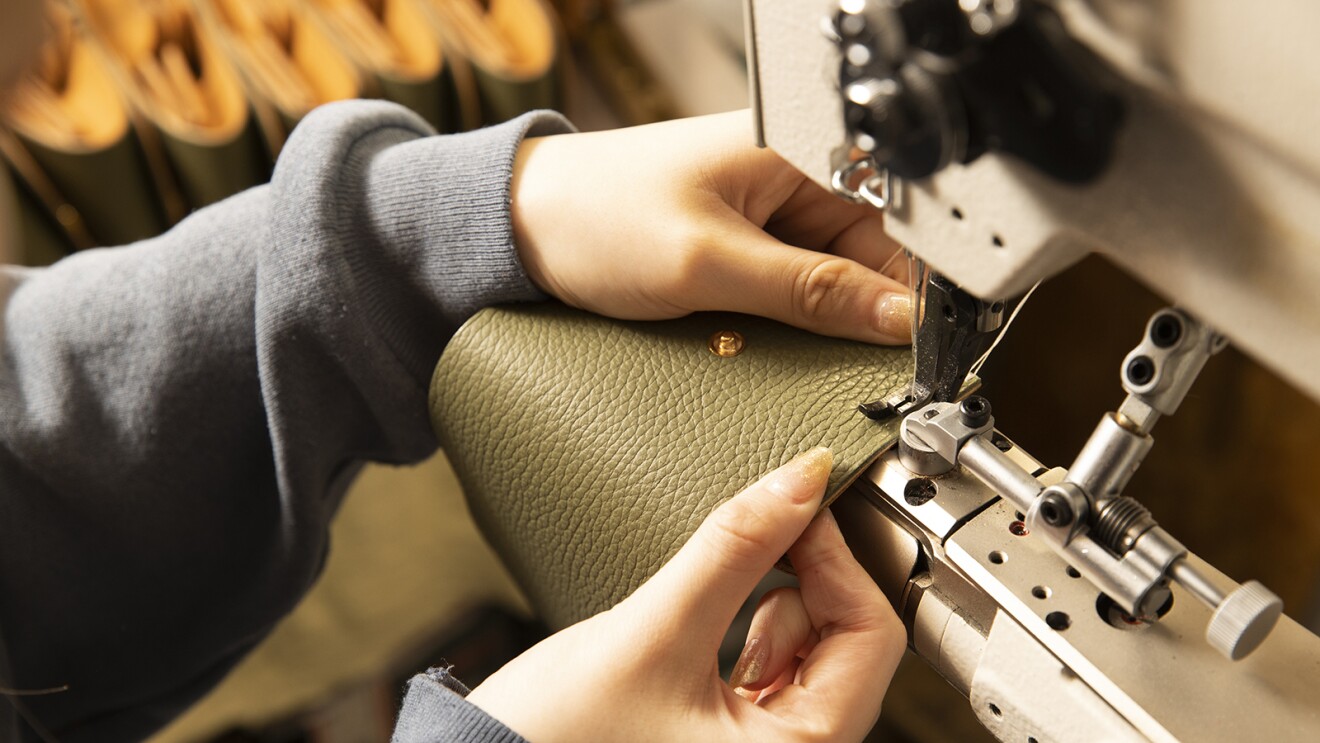 カットや染色が終わりボタンもついた革の縁をミシンで縫っている写真