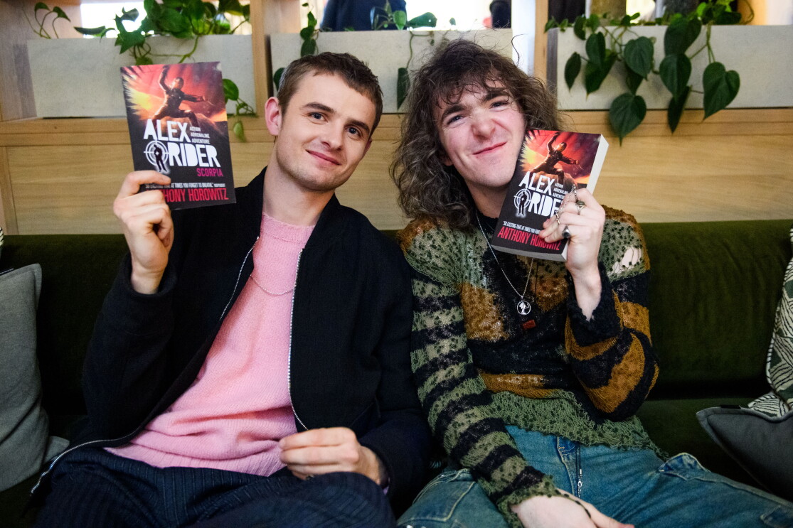 Two men on a sofa holding Alex Rider books