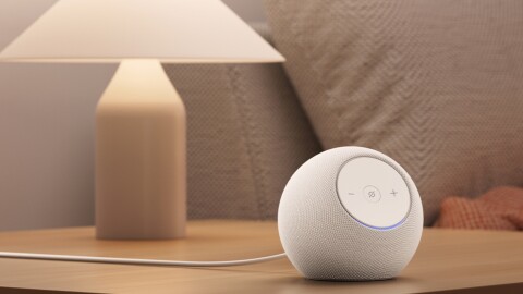 Amazon Echo White on Bedside table next to a bed and a switched on lamp