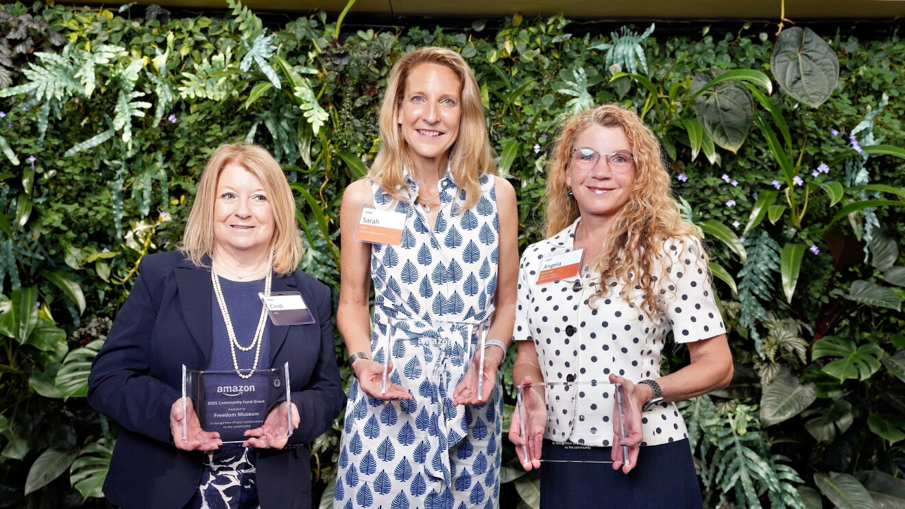 Three women holding awards at Amazon event with lush plant backdrop