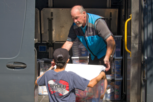 A volunteer handing a bin of donated items to an Amazon delivery driver in a delivery van.