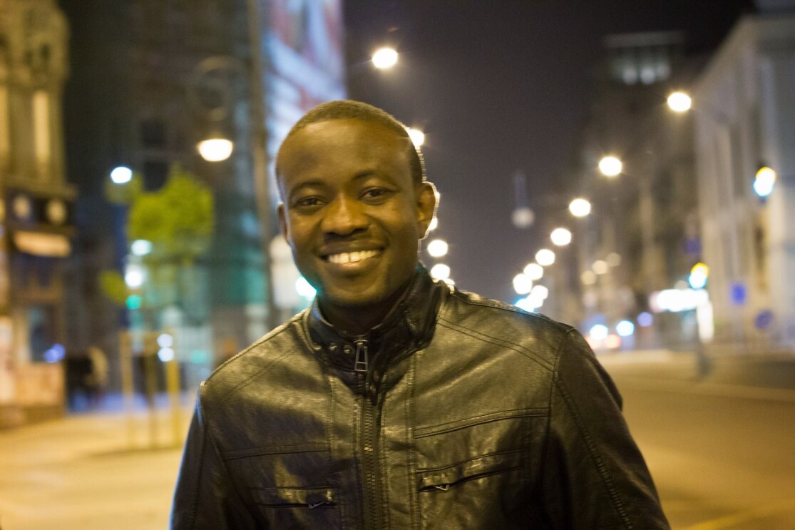 A headshot of a man smiling for the camera with a street in the background.