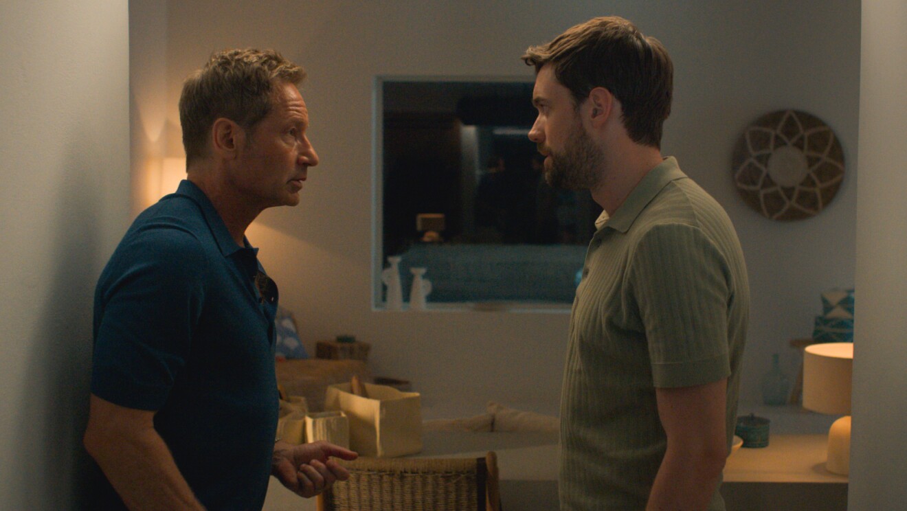 Two men in serious conversation in a dimly lit room
