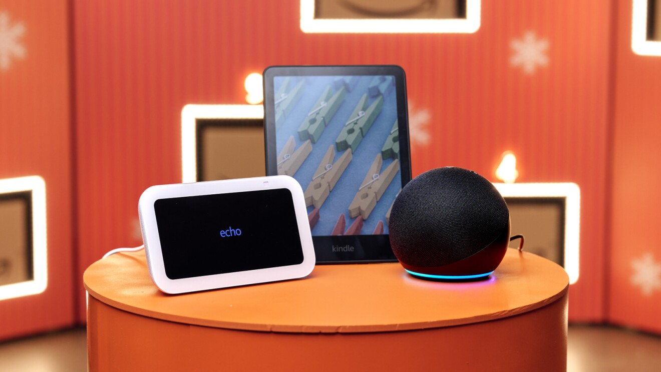Black Friday Amazon Devices (Amazon Kindle, Amazon Dot, Amazon Echo) on an orange table with a festive amazon background
