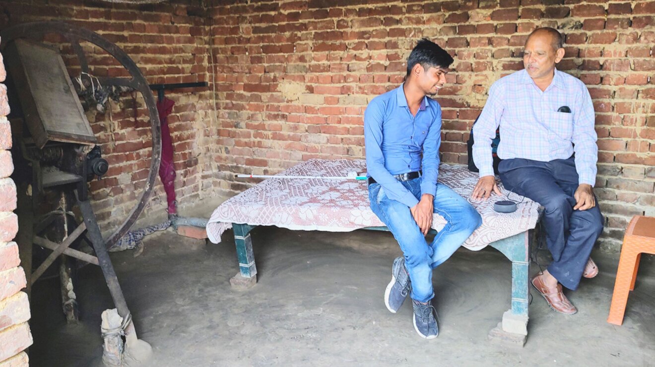 An image of two men sitting on a wide table using an Echo device. 