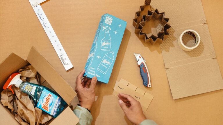 Hands assembling cardboard box amidst clutter on table