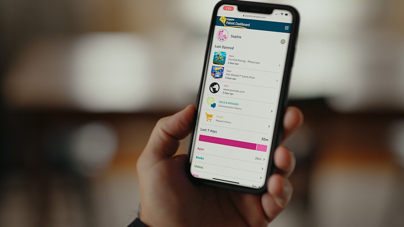 一个人右手拿着一个移动设备。显示屏上有一个Amazon Parent Dashboard。