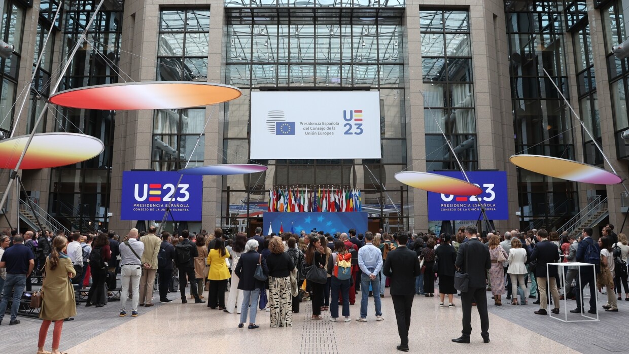 Entrada del Consejo de Europa con gente entrando y de fondo el cartel de la Presidencia Española.