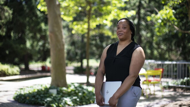 一名穿着牛仔裤和背心的女子双臂抱着笔记本电脑,看着镜头。