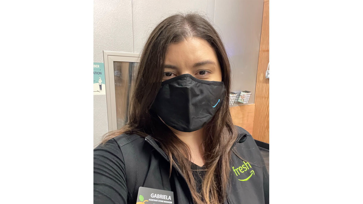 An image of a woman smiling behind a mask for a selfie photo. Her mask has the Amazon logo in the bottom right corner.