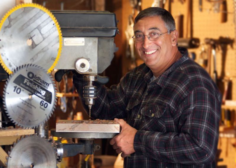 A man stands next to an electric saw and smiles at the camera