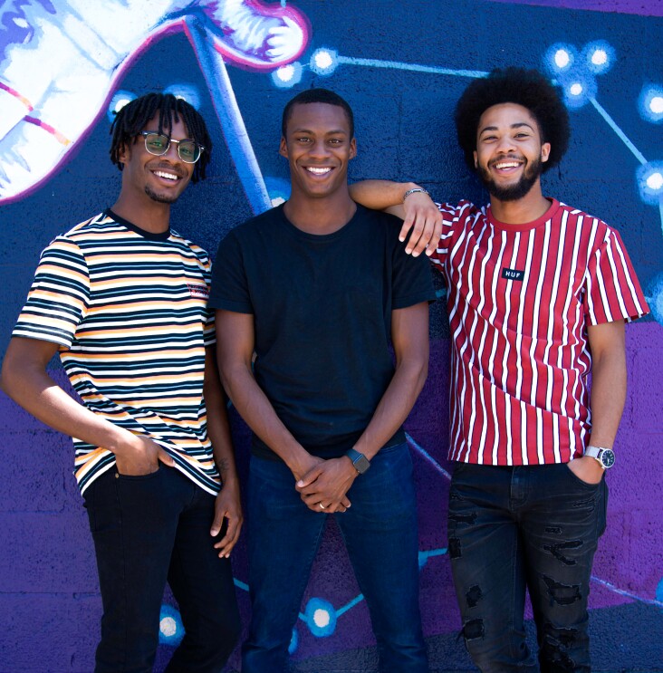 Three AfroPick founders stand side-by-side in front of art.