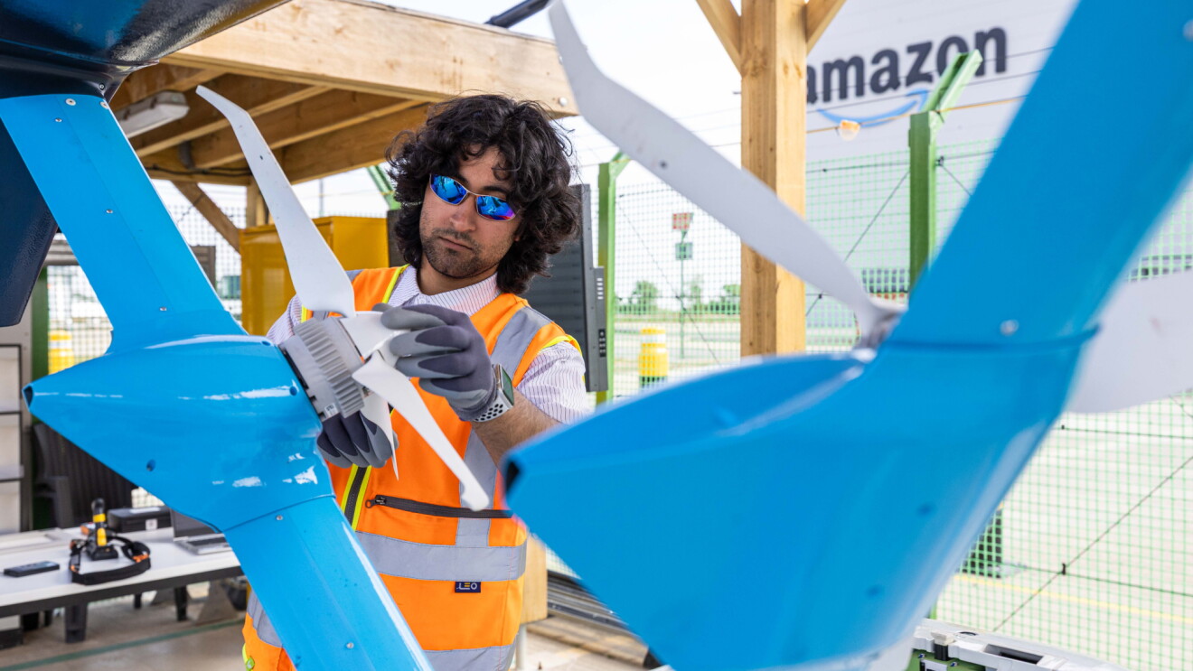 Worker in safety vest inspecting blue drone propeller at Amazon facility