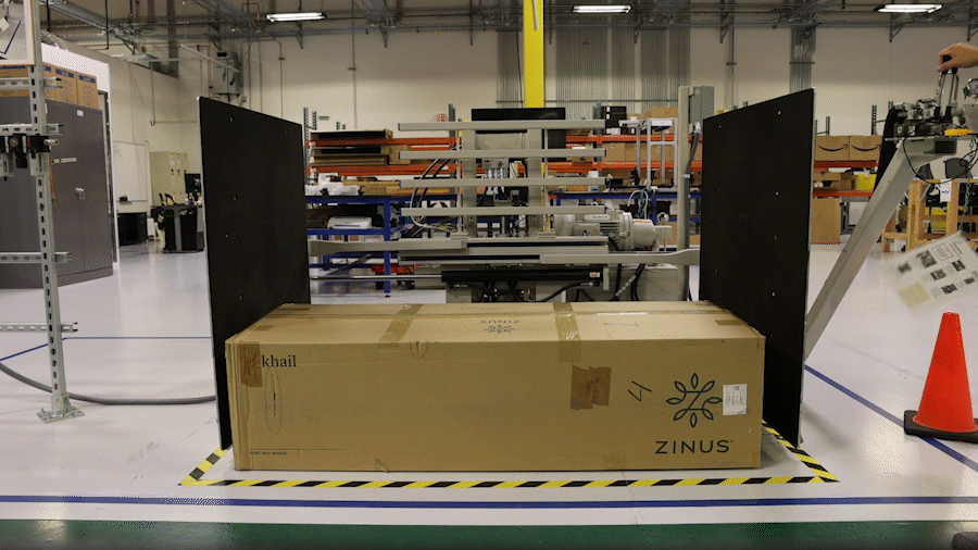 An animated GIF of a large, rectangular box being squeezed by two, big metal plates imitating a fork lift.