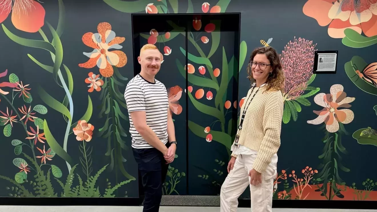 深い緑色をベースに、植物のモチーフが描かれたエレベーターホールの前に立つ男性と女性