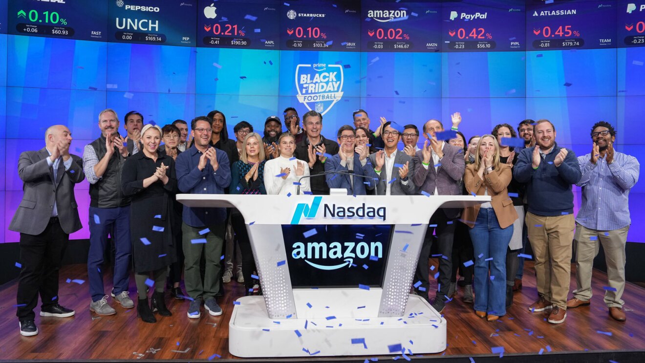 an image of a large group of people standing behind a podium that says "Nasdaq" and "Amazon." they are smiling and clapping while confetti falls around them. There is a blue background behind them that says "Prime Black Friday Football" with the NFL logo.