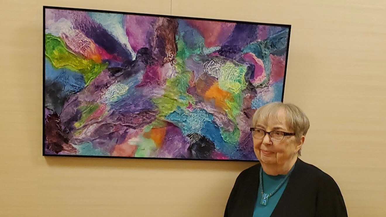 A woman stands in front of a colorful piece of art hanging on a wall.