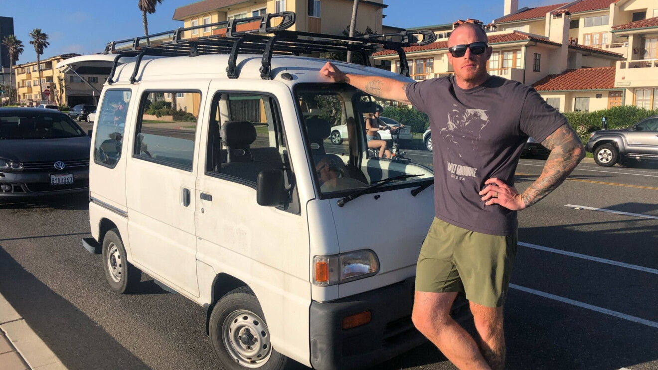 Josh Palacios leans on the front of a white van parked outside.